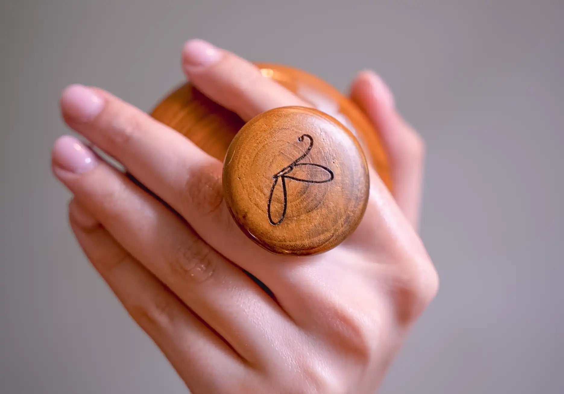 Image of Wooden scalp massager with a unique design and kansa metal held in a hand against a neutral background